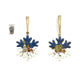 Two snowflake-shaped Christmas ornaments with a blue top half, white bottom half, and a small colorful village scene in between, hanging from gold strings. 