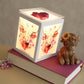 A glowing white cube-shaped wax warmer with painted Highland cow artwork on its sides, displayed on top of a magenta book with a small Highland cow figurine beside it.
